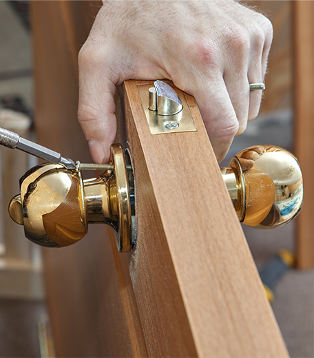 Locksmith fitting a brass doorknob on a wooden door