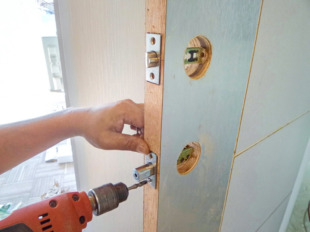 Locksmith using a power drill to install a lock on a door